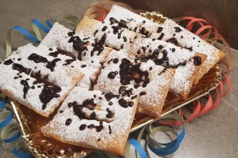 Chiacchiere morbide cosparse di zucchero a velo e gocce di cioccolato, pronte per festeggiare il Carnevale.