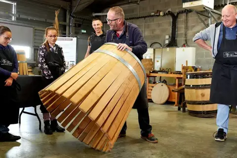 Visite tonnellerie Bourgogne : un maître tonnelier montre un fût en cours de fabrication à des apprentis.