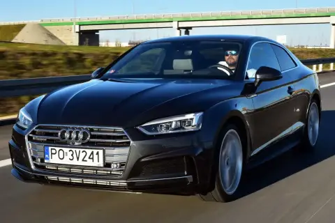 Czarny Audi A5 2025 z kierowcą w okularach przeciwsłonecznych jedzie po autostradzie.