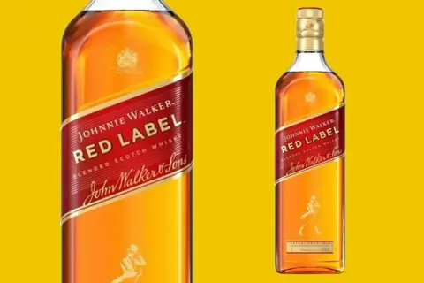 Dwie butelki whisky Johnnie Walker Red Label na żółtym tle. Klasyczna, rozpoznawalna etykieta z czerwonym pasem i postacią spacerowicza.