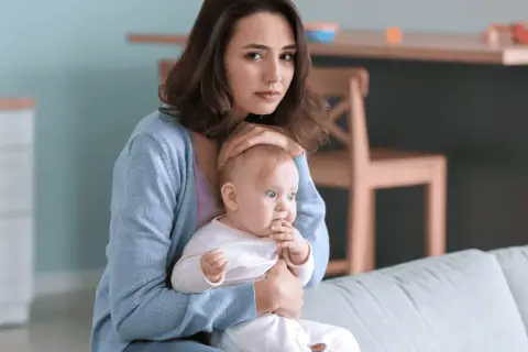 Smutna młoda mama tuli dziecko, czując się przytłoczona. To może być depresja w ciąży, która dotyka wiele kobiet.