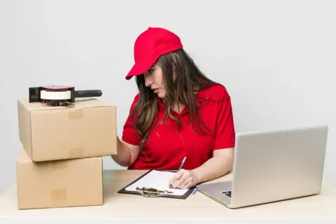 Kurierka przygotowuje paczkę do Kanady, sprawdzając dane na laptopie i notując coś na kartce.