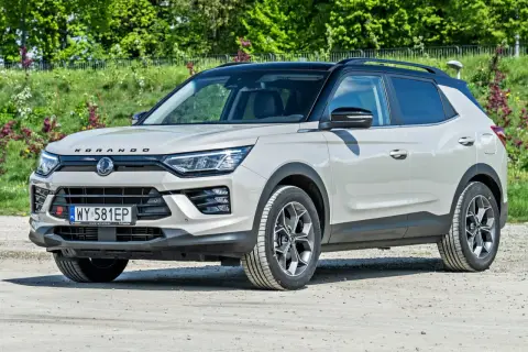 Jasnoszary SsangYong Korando z czarnym dachem stoi na drodze gruntowej, otoczony zielenią.