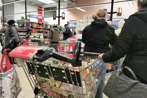 Ludzie robią zakupy w supermarkecie, zastanawiając się, czy w Wielką Sobotę można pracować. Wózek sklepowy pełen produktów.