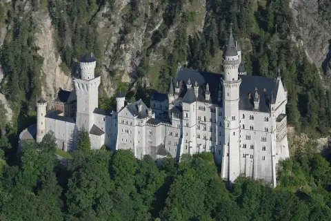 Bajkowy zamek w Niemczech, Neuschwanstein, wyrasta z zielonych lasów na tle skalistego zbocza.
