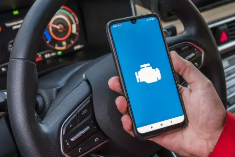 Dacia Sandero z ikoną silnika na ekranie telefonu, gotowa do diagnostyki OBD.