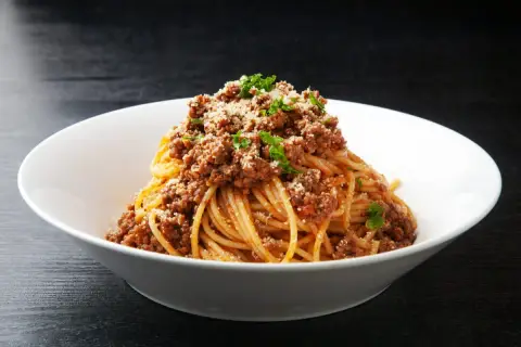 Pyszne spaghetti z bogatym sosem bolognese, posypane parmezanem i natką pietruszki. Idealne danie z makaronem z mięsem mielonym.