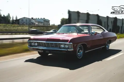 Czerwony Chevrolet Impala 1967 sunie po drodze, błyszcząc w słońcu. Klasyk w ruchu.