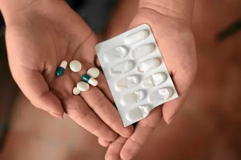 Dłonie trzymające tabletki i blister. Jedna z nich zawiera leki, które mogą być **inhibitory pompy protonowej**, stosowane w leczeniu problemów żołądkowych.