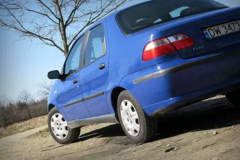 Niebieski Fiat Albea na tle drzew i błękitnego nieba.