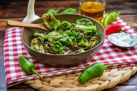 Gebratene Pimientos de Padrón, ein einfaches und leckeres Rezept. Mit grobem Salz bestreut, serviert mit Olivenöl und frischen Kräutern.