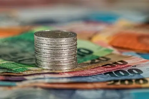 Stos monet na tle kolorowych banknotów.