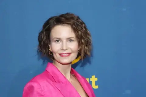 Magdalena Kumorek w różowej marynarce, uśmiechnięta na tle niebieskiego baneru.