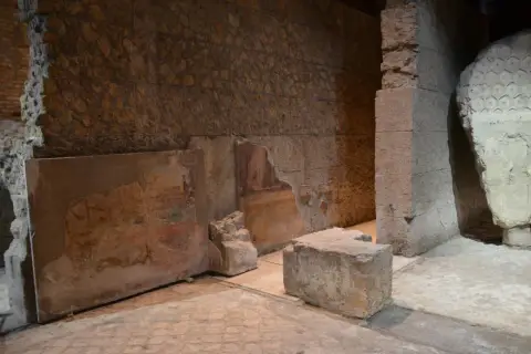 Vestiges d'une fresque murale dans la maison d'Auguste à Rome, avec des blocs de pierre et des murs en ruine.