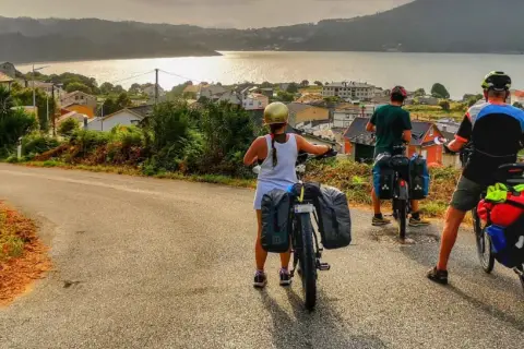 Ciclistas con alforjas exploran **rutas bicicleta** con vistas a un pueblo costero y el mar al atardecer.
