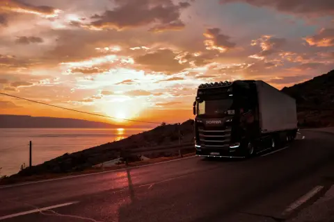 Ciężarówka Scania na drodze przy zachodzie słońca nad morzem. Zastanawiasz się, ile zarabia kierowca tira w Hiszpanii?