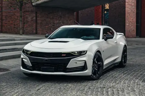 Biały Chevrolet Camaro SS z czarnymi felgami stoi na brukowanej ulicy przed ceglanym budynkiem.