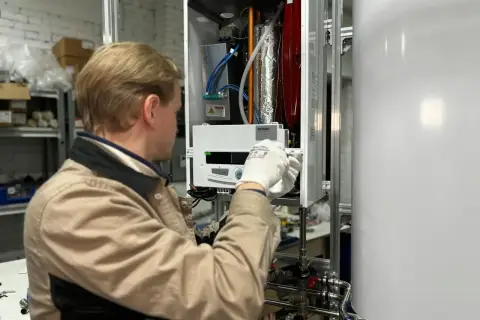 Technik w białych rękawiczkach sprawdza grzałkę miernikiem wewnątrz urządzenia.