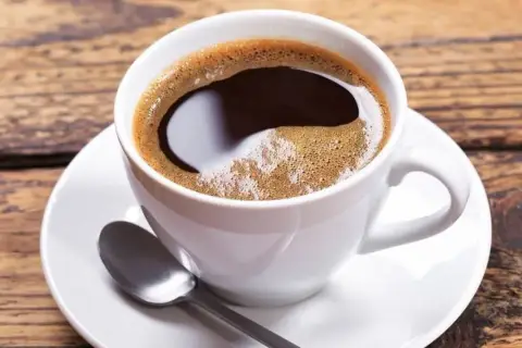 Aromatic coffee in a white cup, perfect for learning jak dobrze zaparzyć kawę sypaną. Na drewnianym blacie leży łyżeczka.
