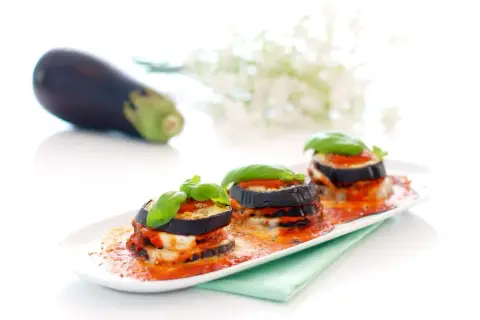Deliciosas berenjenas a la parmesana, apiladas y cubiertas de salsa de tomate y queso fundido, adornadas con albahaca fresca.