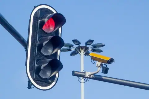 Czerwone światło na sygnalizatorze i żółta kamera monitorująca ruch. Te kamery na sygnalizacji świetlnej dbają o bezpieczeństwo.