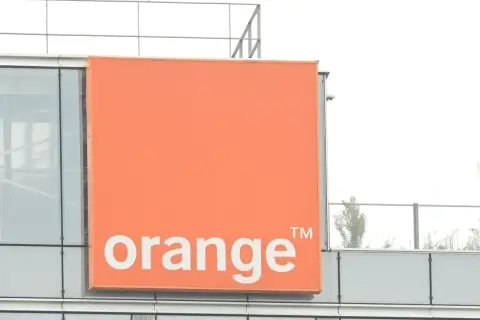 Pomarańczowy znak z napisem "orange" na nowoczesnym budynku. To logo firmy telekomunikacyjnej, która oferuje usługi multiroom.
