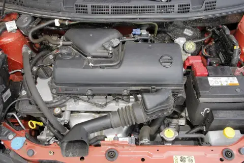 Silnik Nissana Micra K12 z widocznym akumulatorem, przewodami i osłoną silnika.