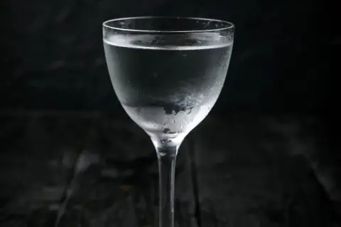 Szklanka z mroźną wódką, pokryta kroplami kondensacji, na ciemnym tle.