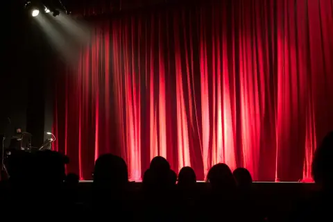 Czerwona kurtyna w teatrze współczesnym w Warszawie. Widownia w mroku, światło reflektora na scenie.
