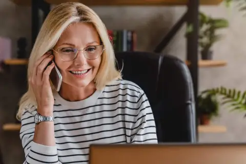 Uśmiechnięta blondynka w okularach rozmawia przez telefon, szukając pożyczki na telefon od zaraz.