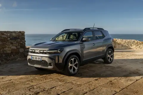Nowy Dacia SUV na tle kamiennego muru i morza.