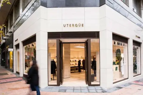 Fachada de tienda UTERQÜE con escaparates y entrada abierta. Una persona pasa por delante.