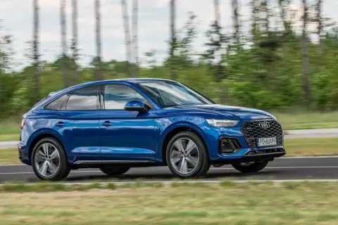 Błękitny Audi Q5 Sportback 2025 pędzi po drodze, otoczony zielenią i drzewami.