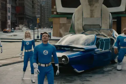 Fantastyczna Czwórka w swoich niebieskich strojach stoi obok futurystycznego pojazdu. Recenzja filmu zapowiada emocjonującą przygodę.