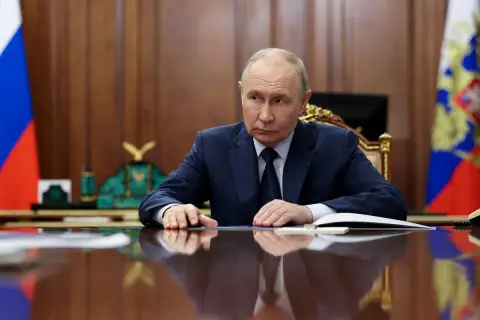 Władimir Putin siedzi przy biurku, zamyślony. Za nim rosyjskie flagi. Czeka na nas świat.
