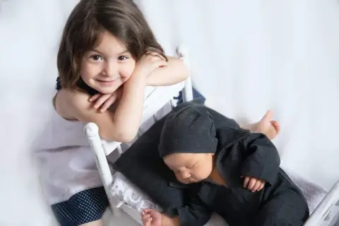 Niña sonríe mientras su hermanito duerme. Quizás ya no habrá rabietas por la llegada de un hermano.