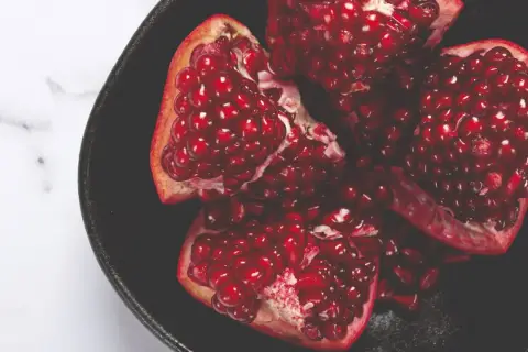 Ein aufgeschnittener Granatapfel in einer schwarzen Schale, voller saftiger Kerne. Ein Symbol für einen gesunden Lebensstil.