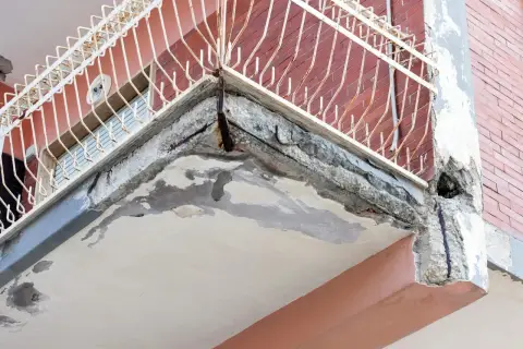 Zniszczony balkon z widocznymi ubytkami w betonie i zardzewiałym zbrojeniem. Idealne miejsce, by zastanowić się, czym uzupełnić ubytki w betonie na zewnątrz.