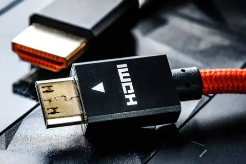 Złote wtyczki HDMI, jedna z nich z czarną obudową i napisem HDMI, połączone z czerwonym, plecionym kablem.