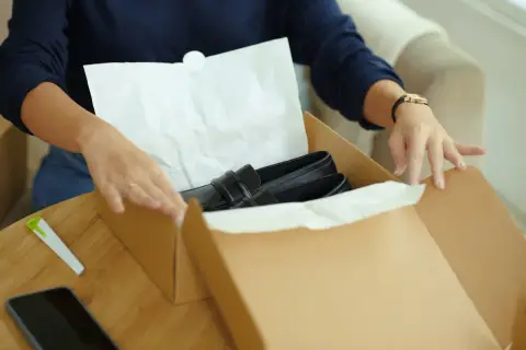 Kobieta przygotowuje zwrot towaru w sklepie stacjonarnym, pakując czarne mokasyny do kartonowego pudełka.