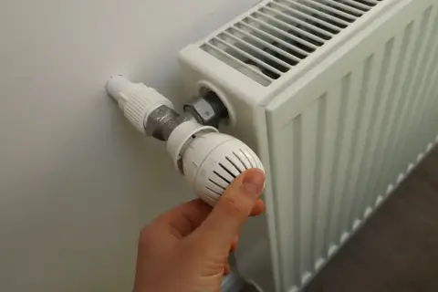 Dłoń reguluje termostat grzejnika. Sezon grzewczy od kiedy do kiedy zależy od pogody i przepisów.
