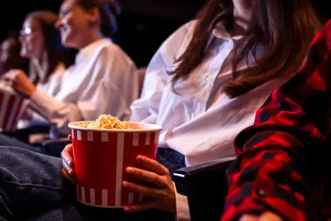 Ludzie w kinie jedzą popcorn. Zastanawiasz się, ile kosztują nachosy w kinie?