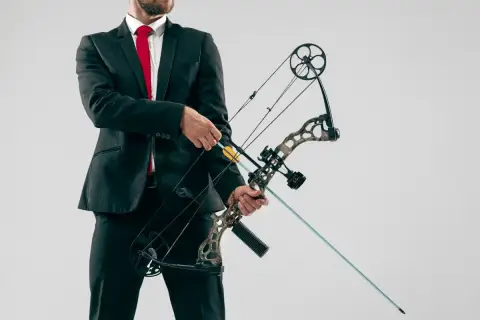 Mężczyzna w garniturze i czerwonym krawacie trzyma łuk rambo z zamontowaną strzałą.