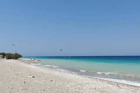 Plaża w zatoce Ialyssos, z turkusową wodą i kilkoma kitesurferami na horyzoncie.