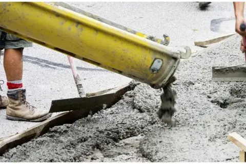 Betoniarka wylewa świeży beton. Pracownicy przygotowują teren, a pytanie "jak długo podlewać beton" jest kluczowe dla jego trwałości.