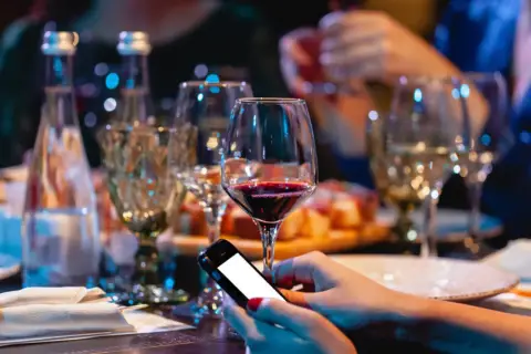 Zanim sięgniesz po alkohol, pomyśl o "podkładzie". Na stole wino, przekąski i telefon. Unikaj skutków picia alkoholu na pusty żołądek.