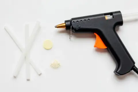 Pistolet do kleju na gorąco, kilka pałeczek kleju, muszelka i żółty krążek. Czy klej na gorąco przewodzi prąd?