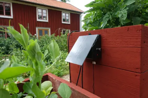 En solcellsdriven bevattning sköter om växterna vid ett rött hus.