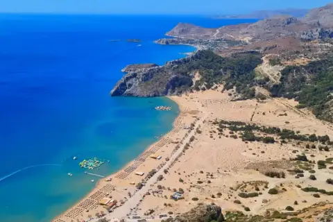 Rodos: turkusowe morze, piaszczysta plaża z leżakami i wodnym parkiem rozrywki, górzyste wybrzeże.