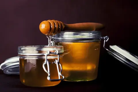Dwa słoiki pełne złotego miodu, z drewnianej chochli spływa słodka kropla.